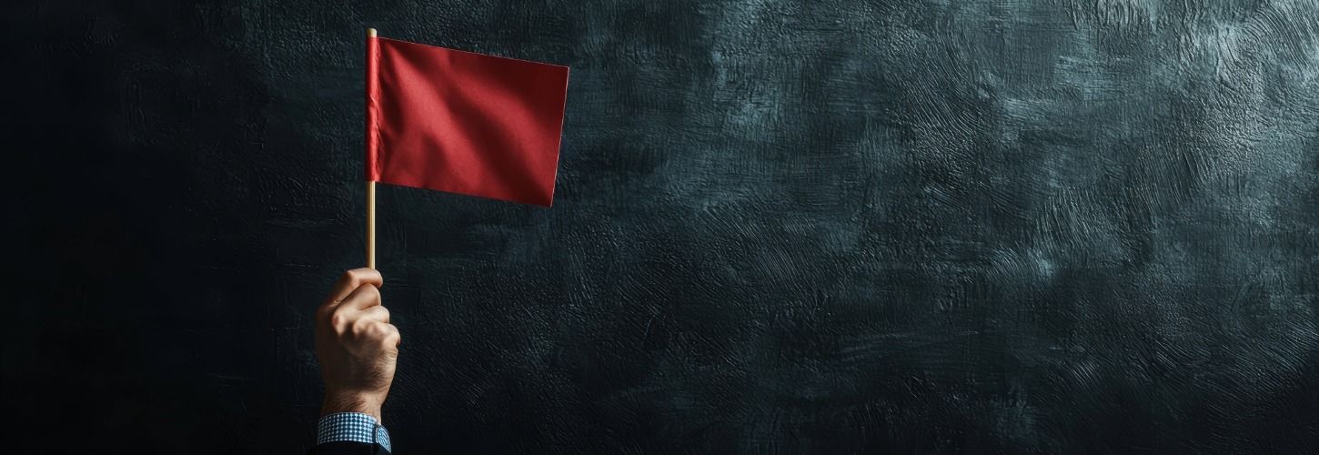 A hand in a suit holds a small red flag against a dark, textured background. The image conveys a warning or alert tone.