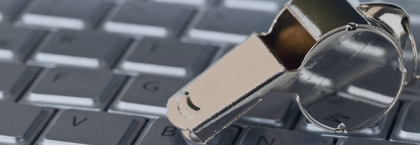A silver whistle rests on a computer keyboard, symbolizing digital whistleblowing. The reflective whistle contrasts with the gray keys, evoking alertness and security.