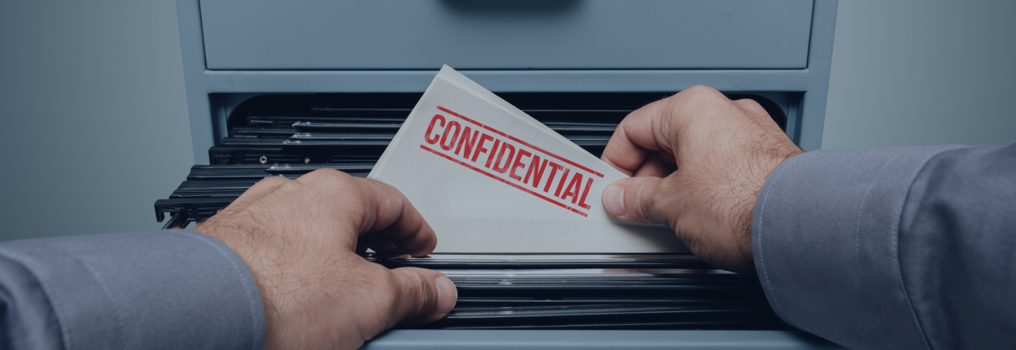 Close-up of a person's hands pulling a white document folder stamped with the word "CONFIDENTIAL" in red ink out of a gray office filing cabinet drawer.