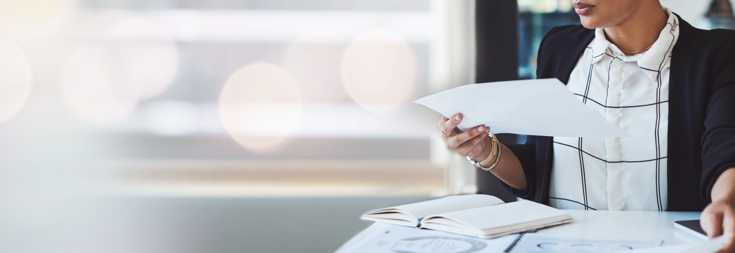 Business professional reviewing paperwork at a desk with an open notebook, representing vendor assessments, compliance reviews, and third-party risk management.
