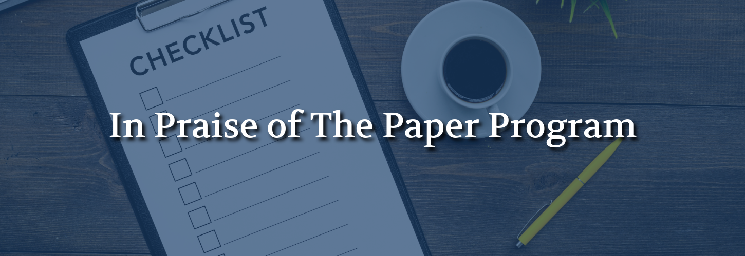 “In Praise Of The Paper Program” displayed over a checklist on a clipboard with a pencil and office workspace.