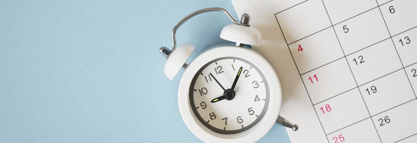 Alarm clock beside a monthly calendar representing compliance deadlines, scheduling, and time management.