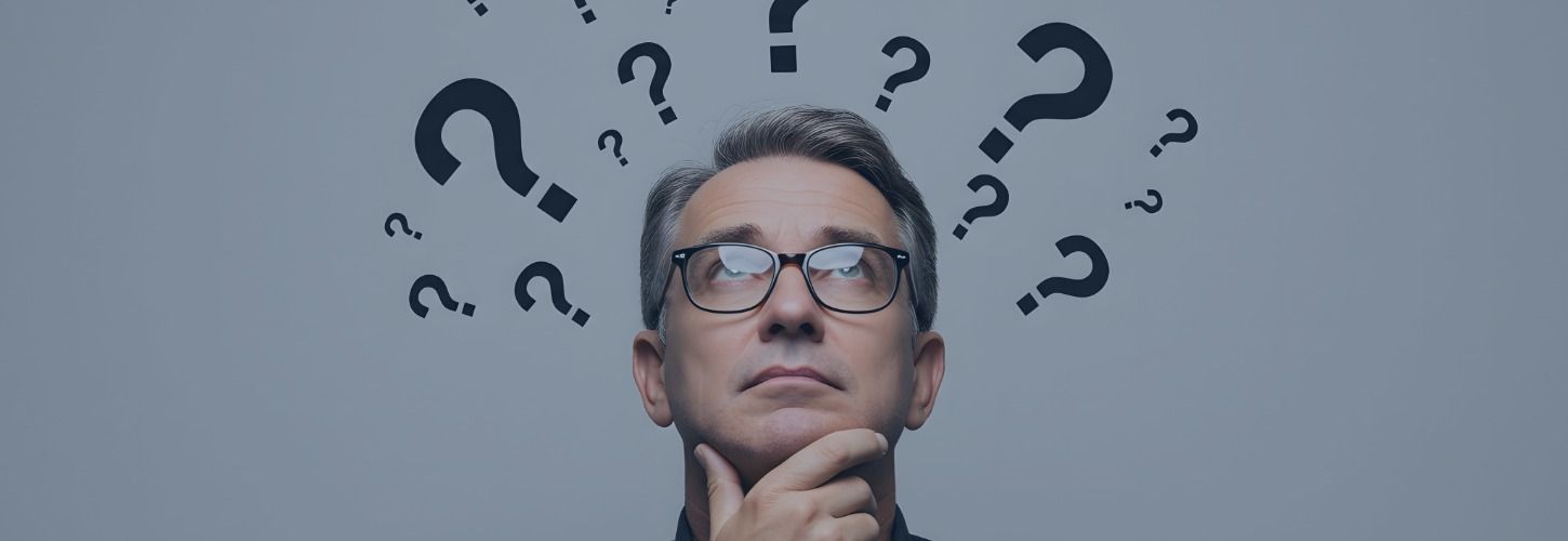 A man with glasses looks up thoughtfully, surrounded by large and small question marks on a gray background, conveying curiosity and contemplation.